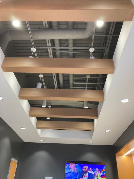 Office ceiling with exposed ducts and wooden beams above a TV screen on a dark wall