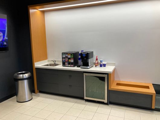Break room counter with coffee machines, sink, trash can, and wooden bench seating