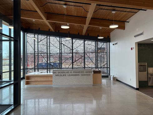 Empty lobby with stone reception desk, large patterned windows, wood ceiling, and tiled floor.