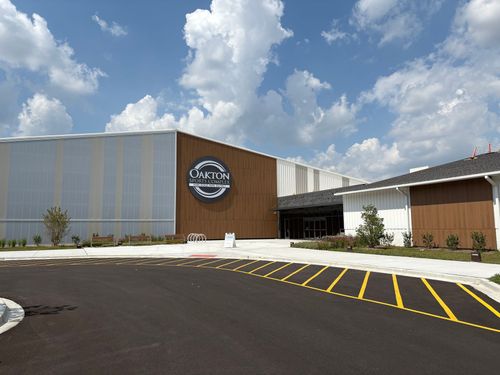 Modern building entrance with a circular sign, brick and white facade, and yellow-striped driveway under a cloudy sky