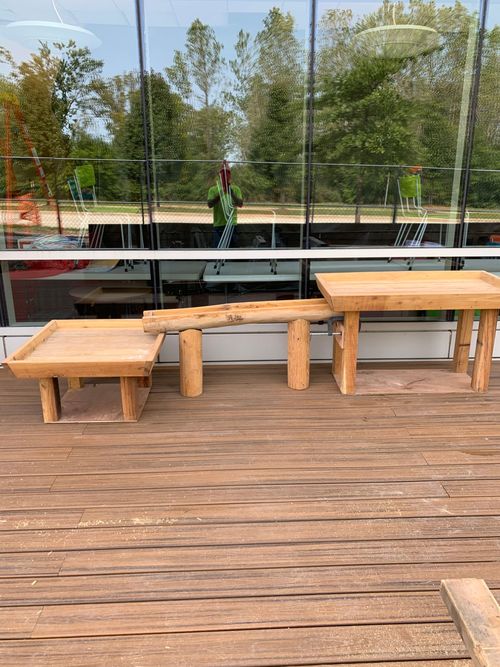 Wooden benches on a deck facing a trampoline court with trees in the background