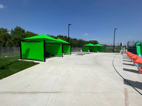 Bright green pop-up tents lining a concrete path beside orange lounge chairs under a clear blue sky