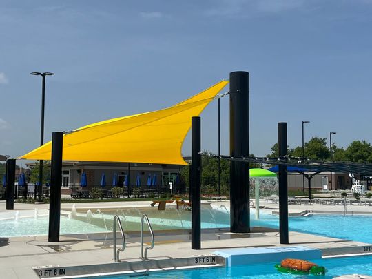 Yellow shade sail over outdoor pool with black posts and clear blue water