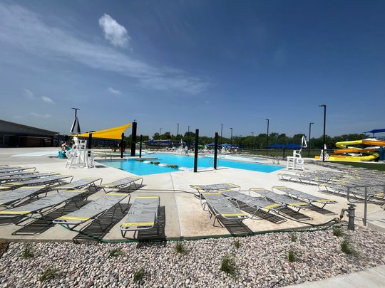 Outdoor pool with lounge chairs, yellow shade sails, and clear blue water under a sunny sky