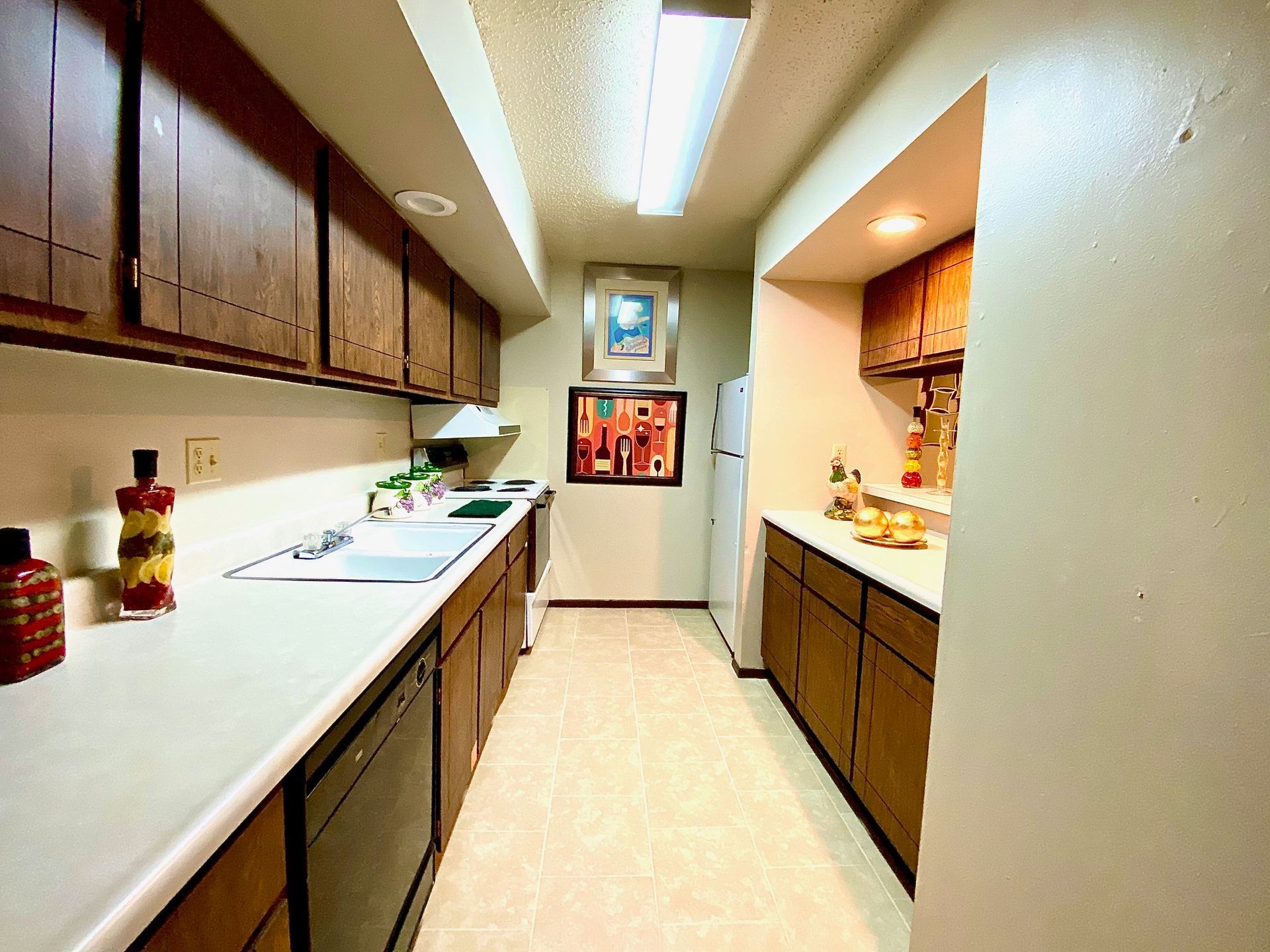 Kitchen with brown cabinets, white countertops, and beige floor. Refrigerator and artwork on wall.