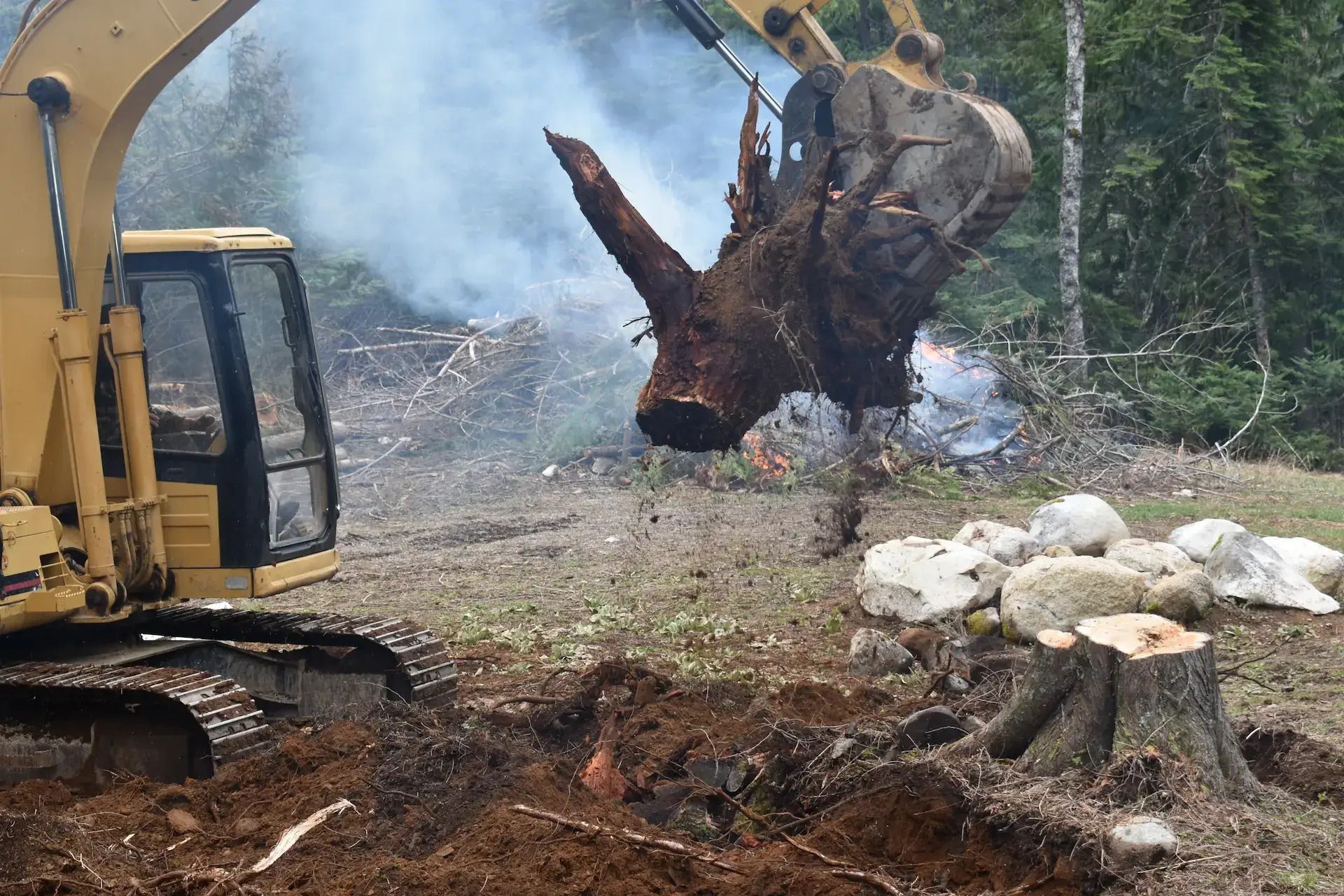 A bulldozer is carrying a large tree stump in its bucket