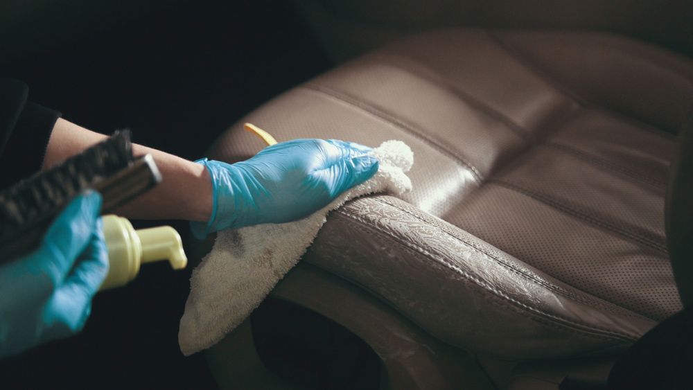 A Person Wearing Blue Gloves is Cleaning a Leather Seat in a Car — Furniture & Auto Pride in South West Rocks, NSW