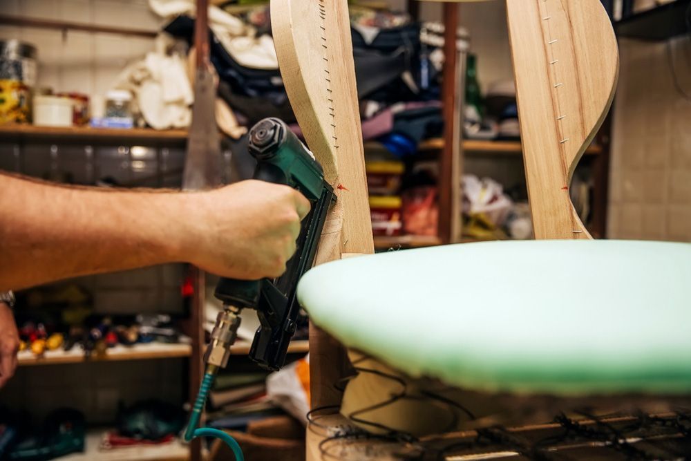 A Man is Using a Stapler to Fix a Chair in a Workshop — Furniture & Auto Pride in Wauchope, NSW