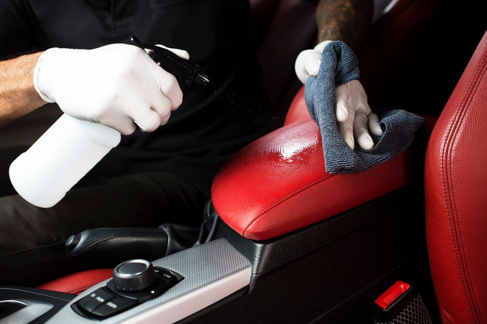 A man is cleaning the interior of a car with a cloth and spray bottle — Furniture & Auto Pride In Port Macquarie, NSW