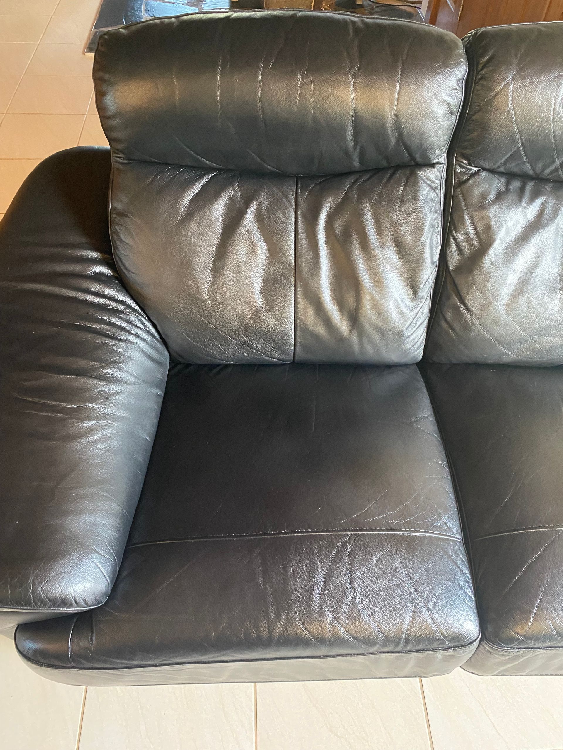A black leather couch is sitting on a tiled floor. — Furniture & Auto Pride In Port Macquarie, NSW