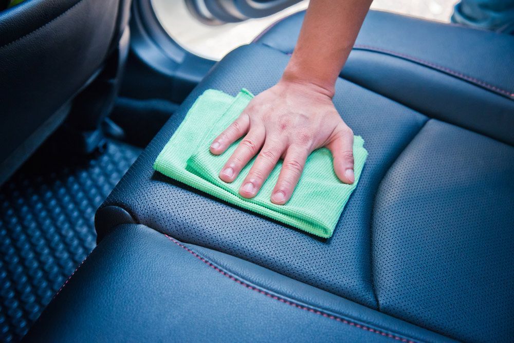 A Person is Cleaning the Back Seat of a Car With a Cloth — Furniture & Auto Pride in Bonny Hills, NSW