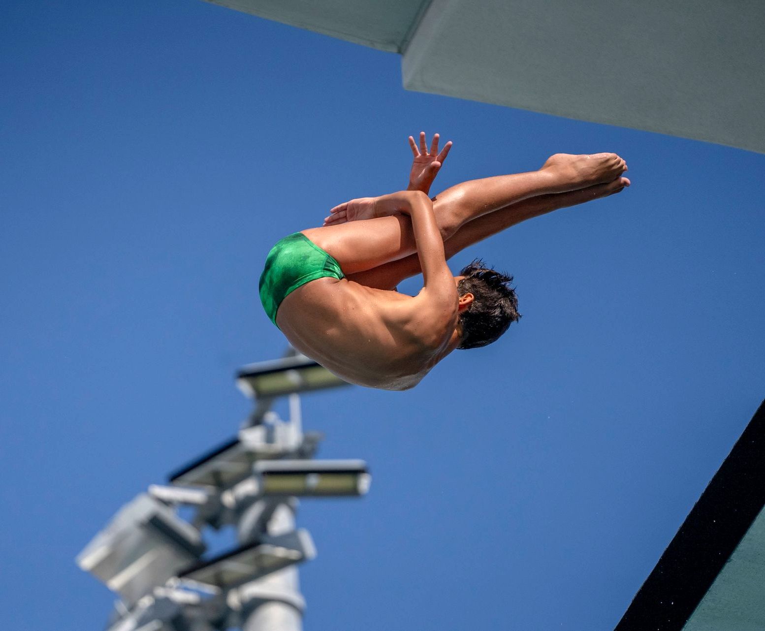 A man in green swim trunks is diving into a pool