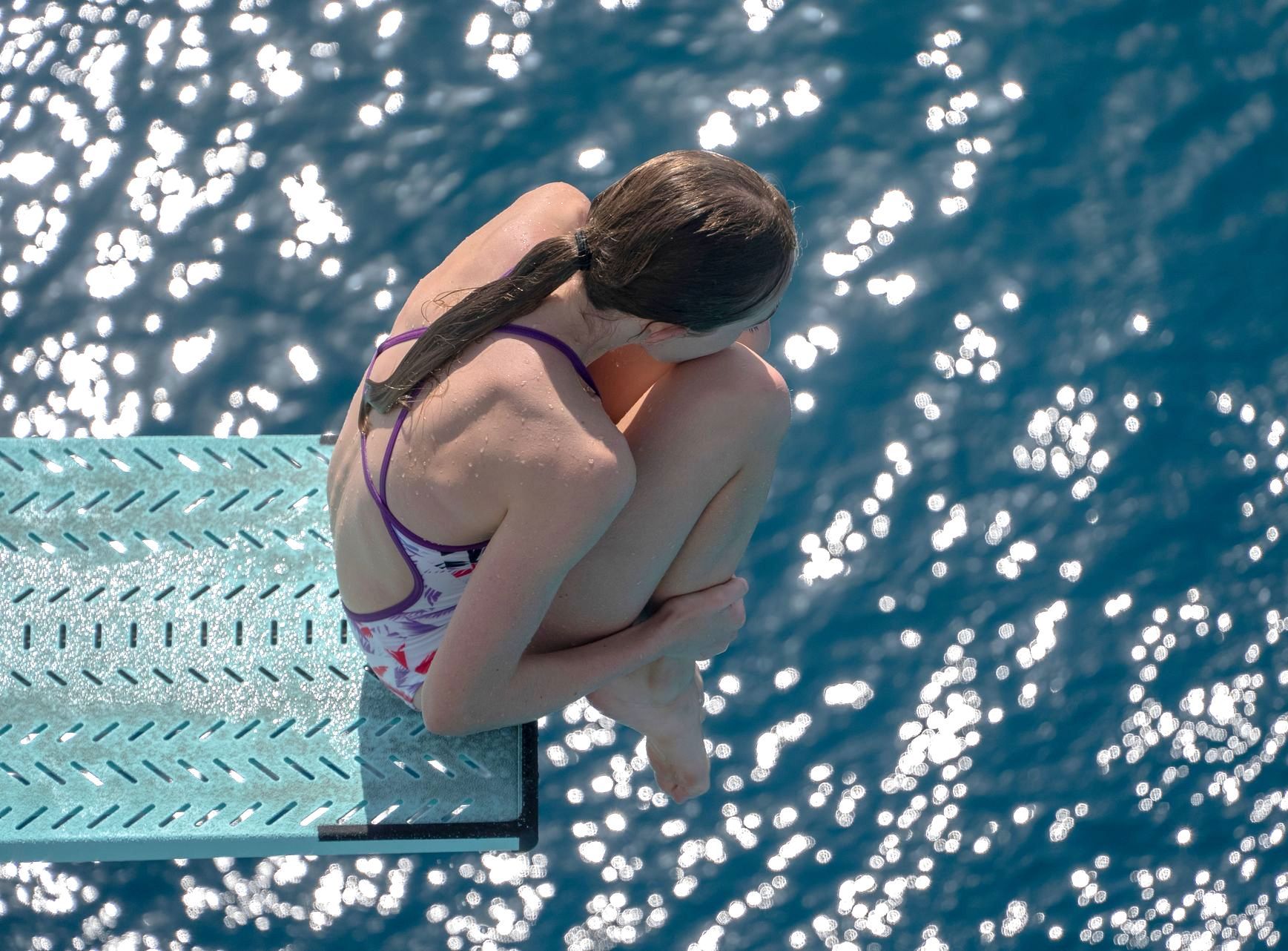 A woman is sitting on a diving board in the water