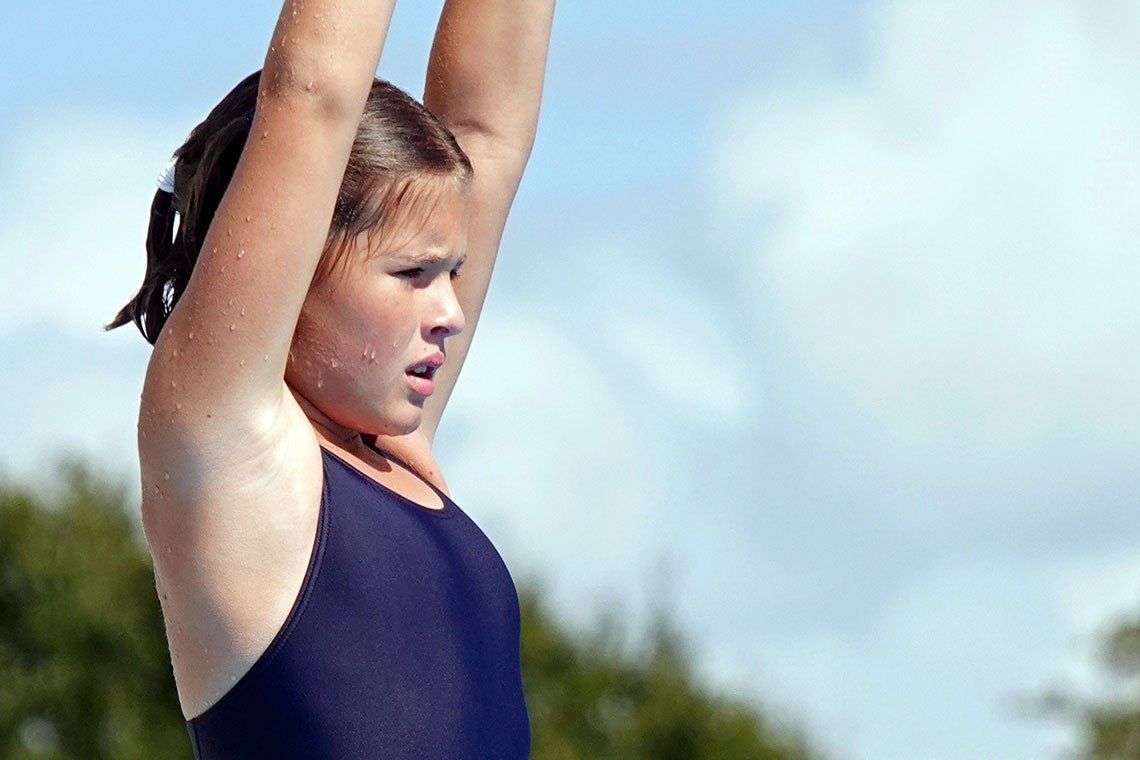 A young girl in a blue swimsuit is raising her arms in the air