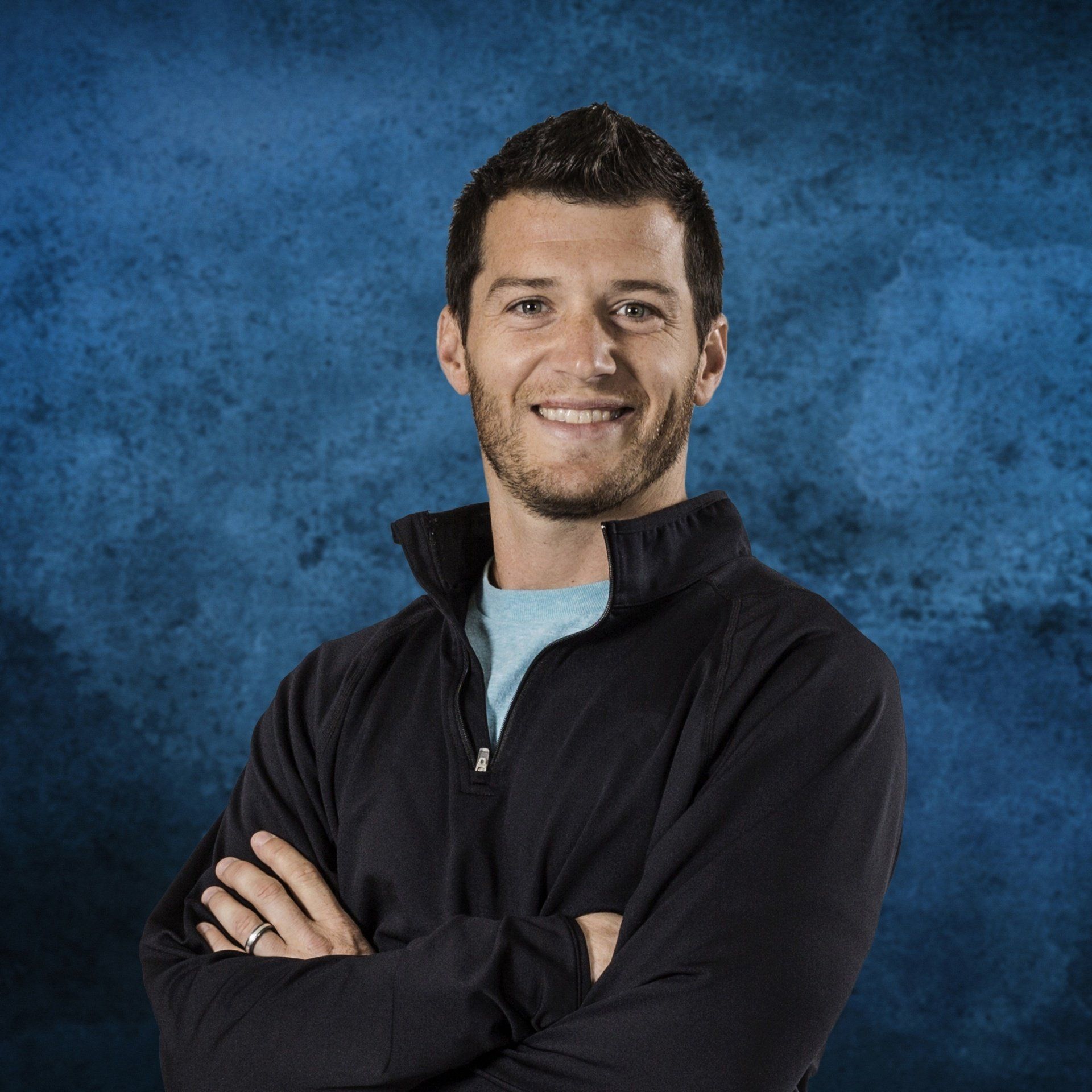 A man with his arms crossed is smiling in front of a blue background