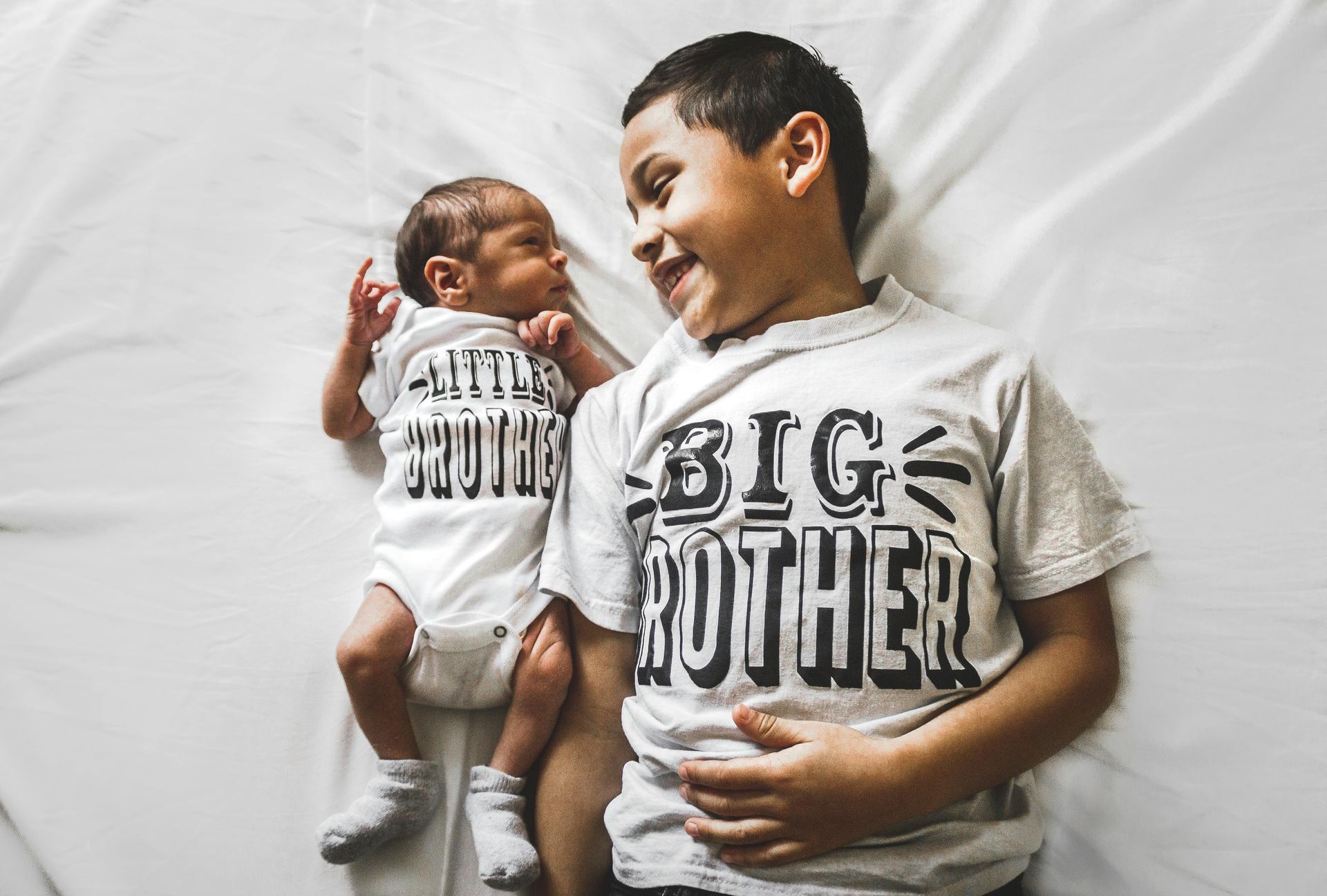 Older boy smiles at newborn brother wearing 