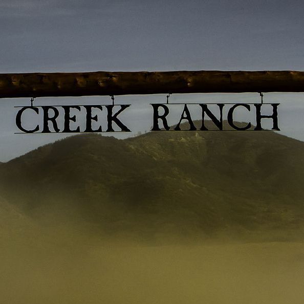 A sign for creek ranch hangs from a fence
