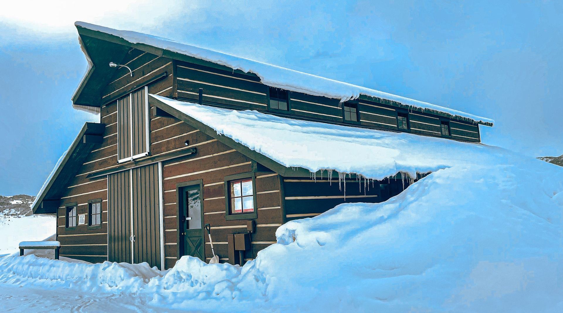 A log cabin covered in snow with a blue sky in the background