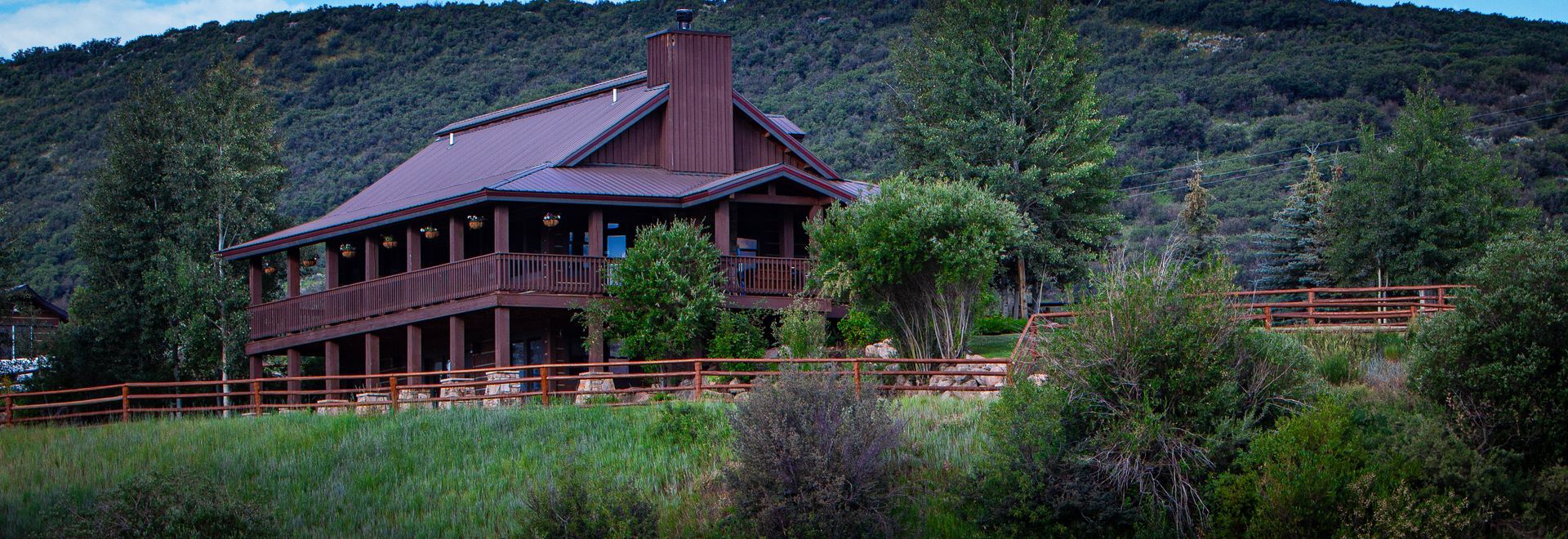 A large log cabin is sitting on top of a hill surrounded by trees.