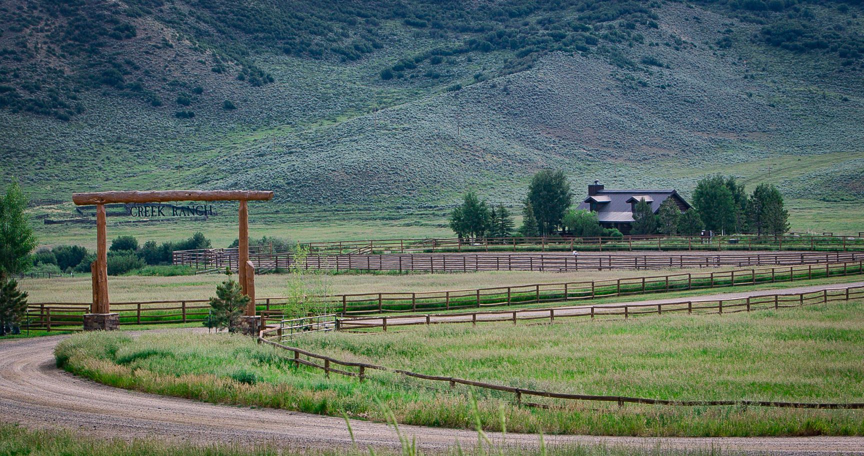 A wooden fence surrounds a grassy field with a house in the background.
