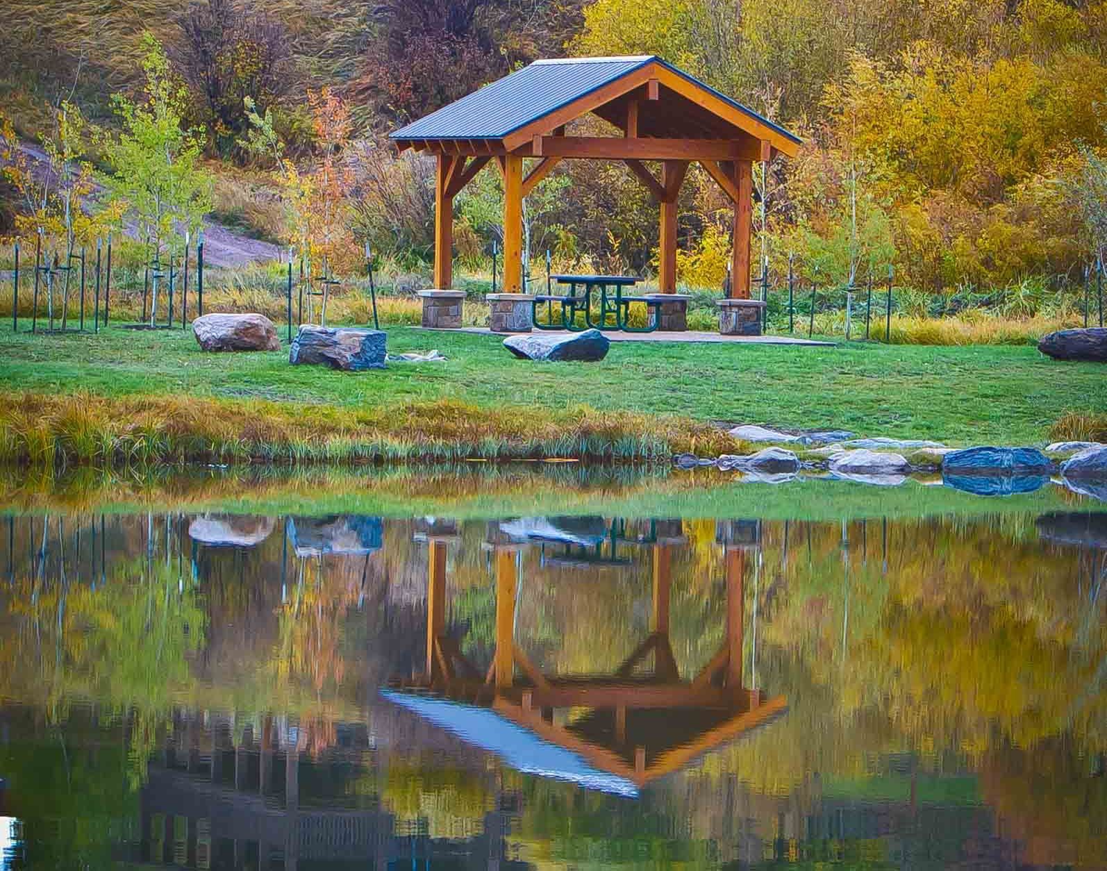 A gazebo in a park is reflected in the water.