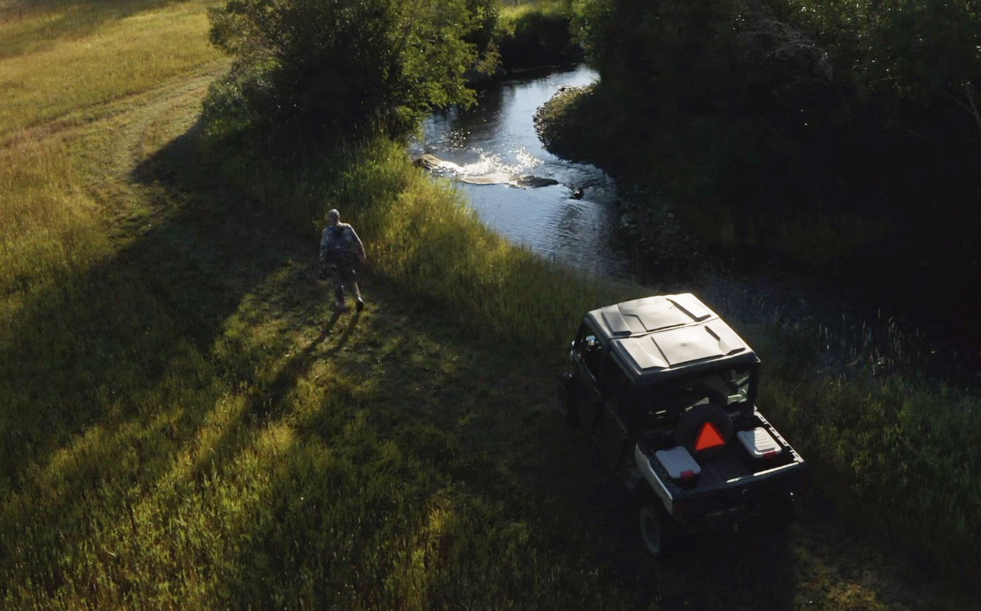 An aerial view of a atv driving down a dirt road next to a river.