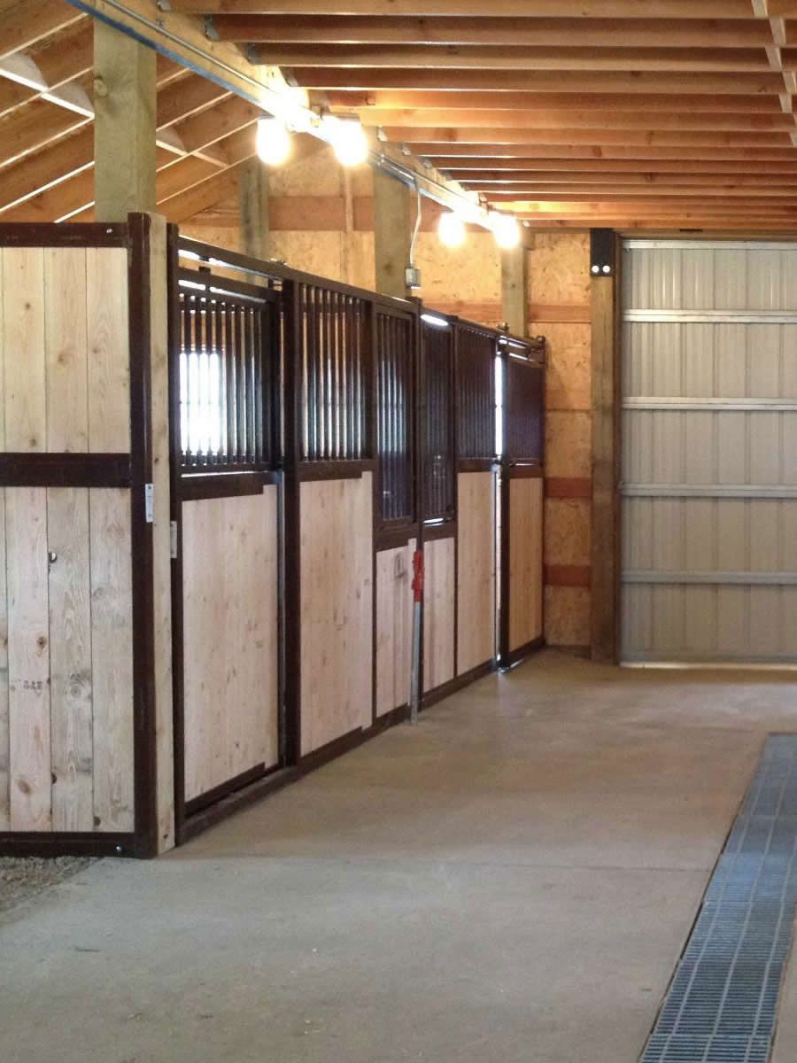 A row of horse stalls in a barn with a garage door