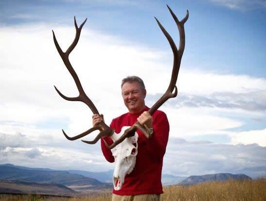 A man in a red shirt is holding a deer skull and antlers