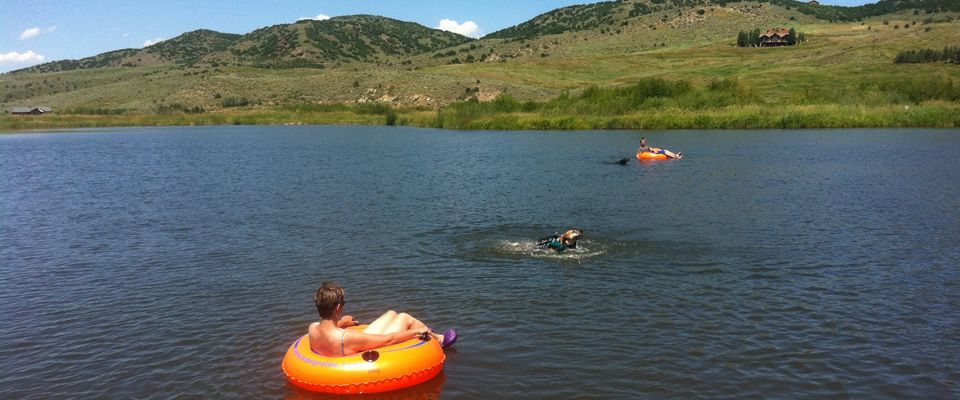 A man in an orange inner tube is swimming in a lake.