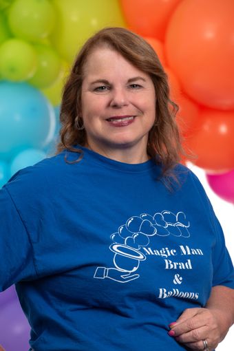 A woman in a blue shirt is standing in front of balloons.