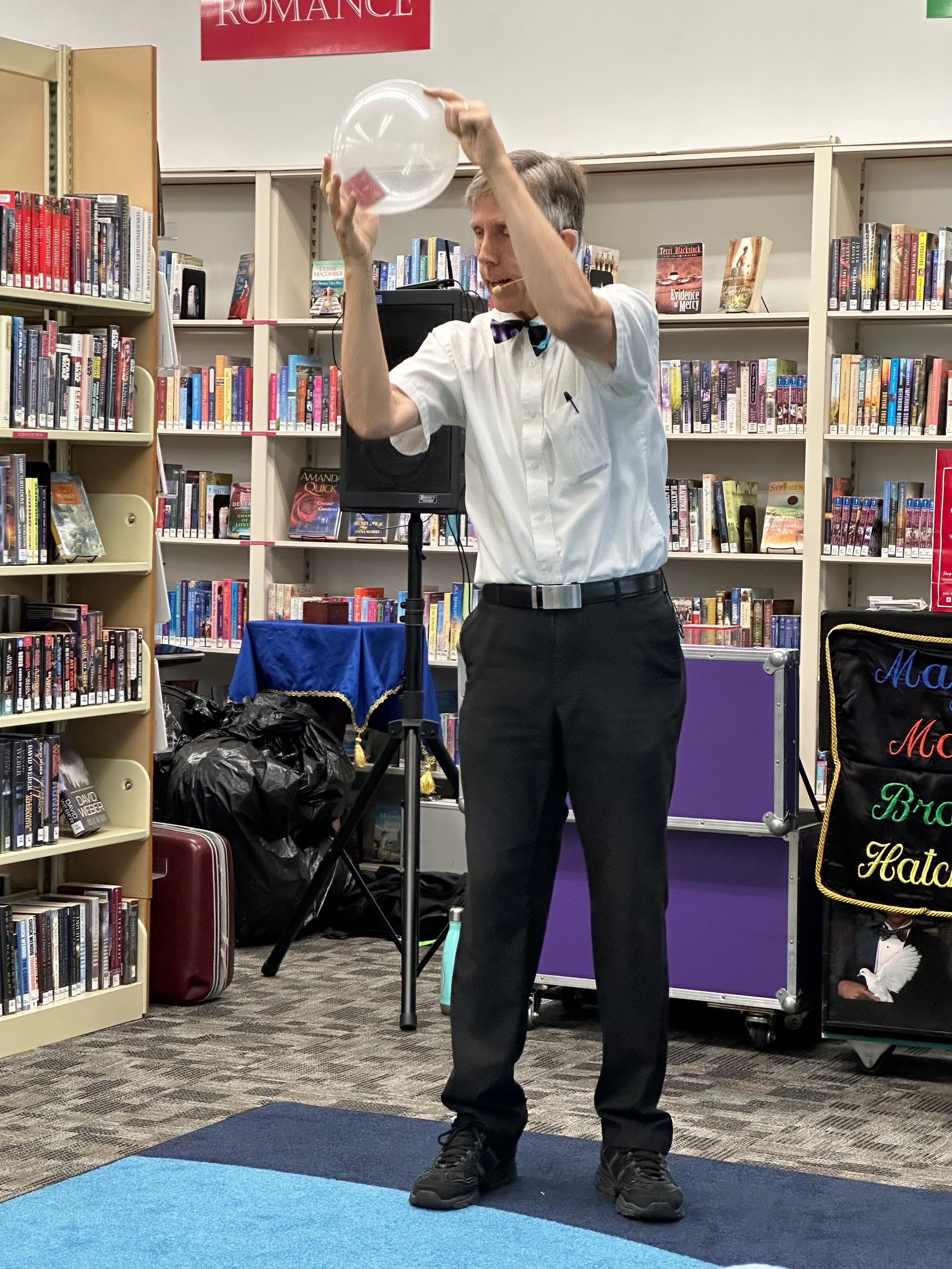 A man in a white shirt and black pants is holding a plastic container in a library.