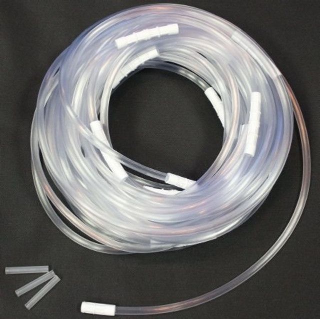 Coiled clear tubing with several white connectors and three small tube pieces on a black surface.