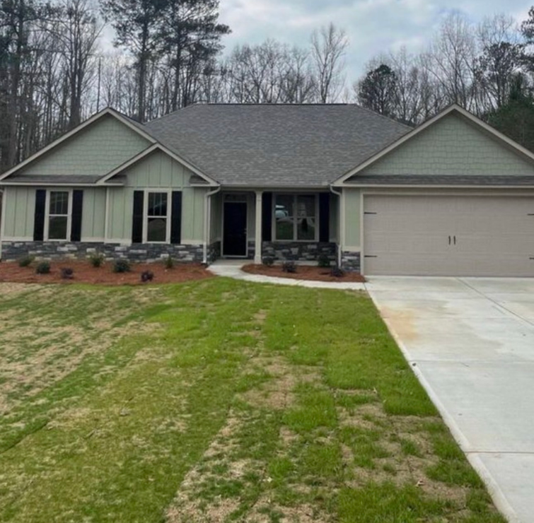 Two-story tan house with white garage door, stone accents, and blue sky.
