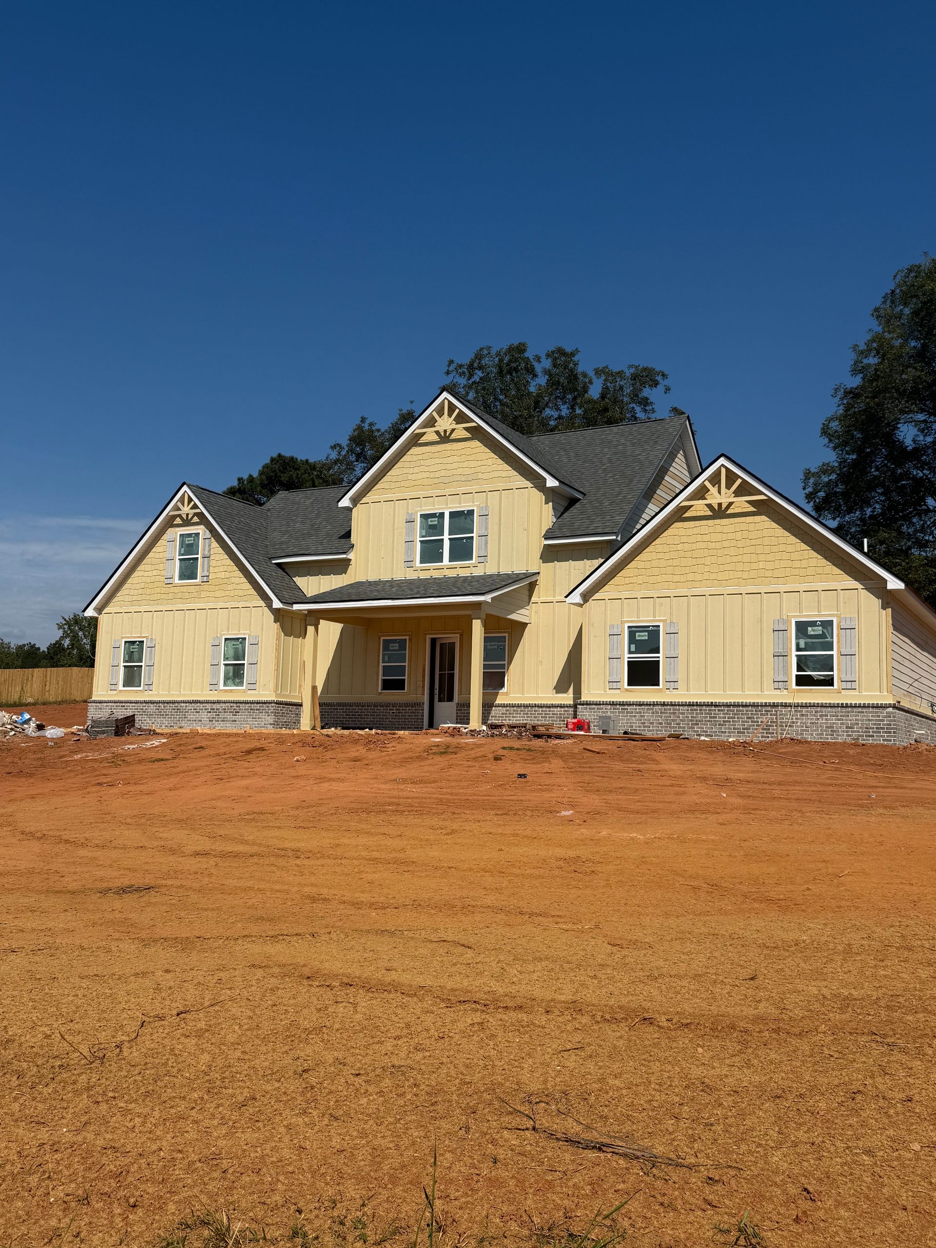 New house under construction with light yellow siding and a gray roof on a sunny day.