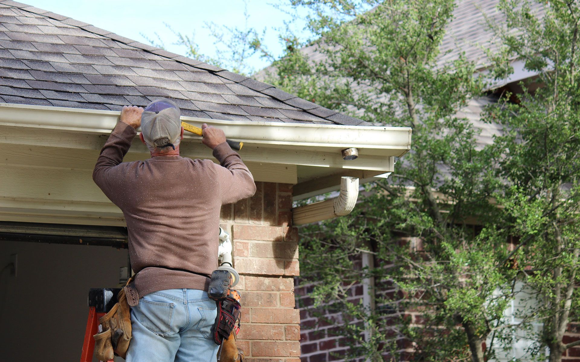 Man on ladder repairing a gutter on a brick house.
