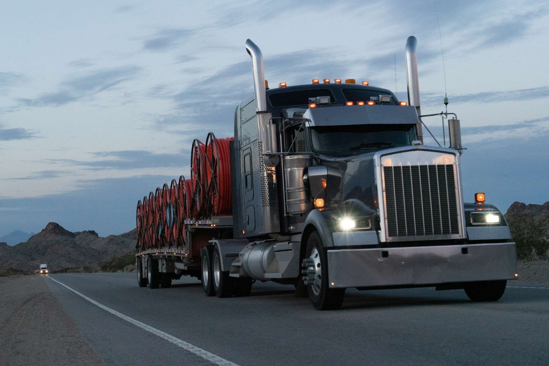 Semi-truck hauling large cable spools on flatbed trailer at dusk on highway. Semi-truck hauling large cable spools on flatbed trailer at dusk on highway.