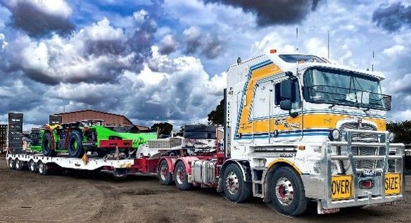 Large white and yellow truck towing a flatbed trailer carrying a bright green vehicle.
