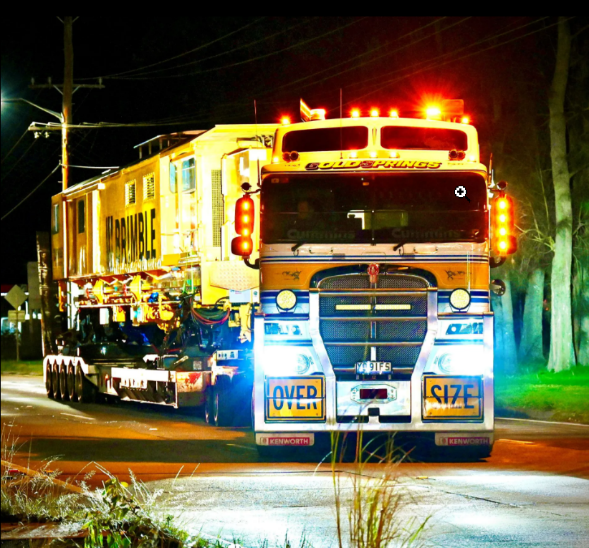 An over-size truck travelling down a dimly lit road with headlights shining brightly in the night.