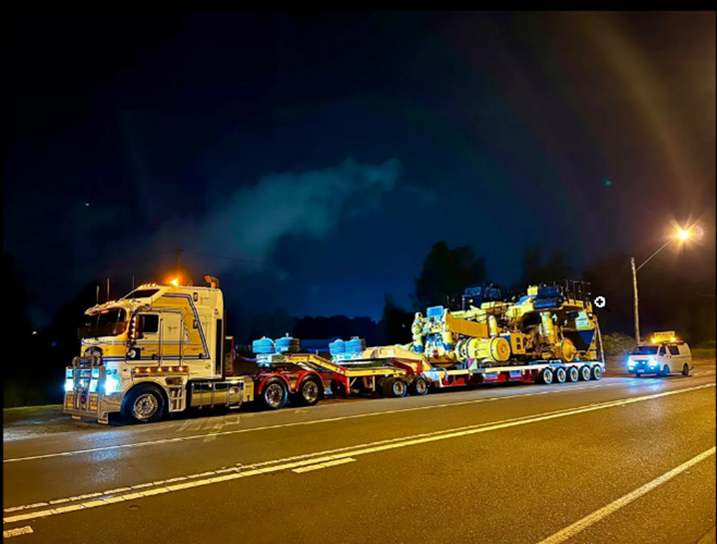 A heavy-duty truck with a crane on its truck bed, with headlights shining brightly in the night.
