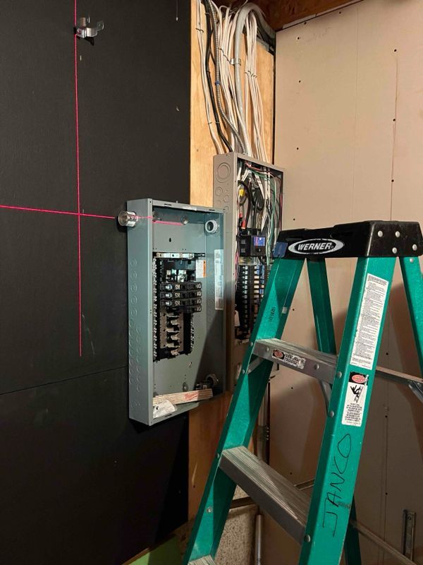 A green ladder is leaning against a wall next to an electrical box.