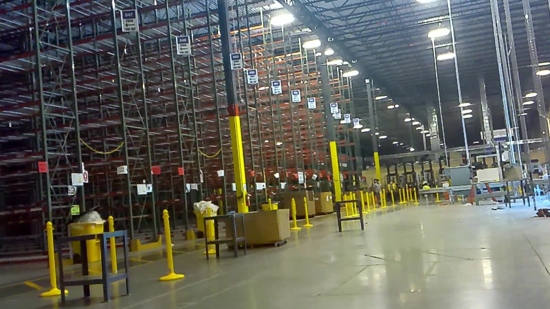 A large warehouse with lots of shelves and yellow poles.