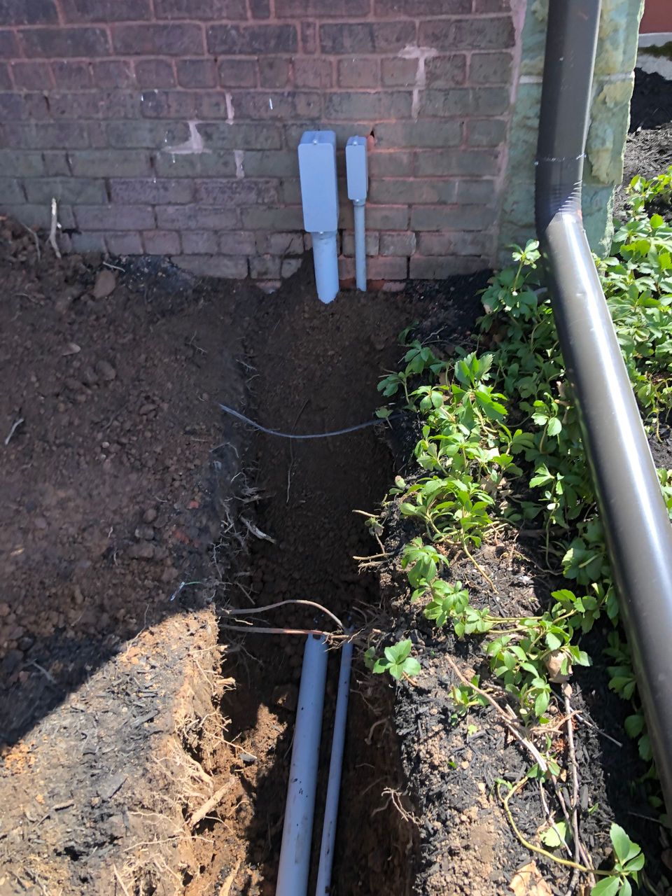 A drain pipe is being installed in the dirt near a brick wall