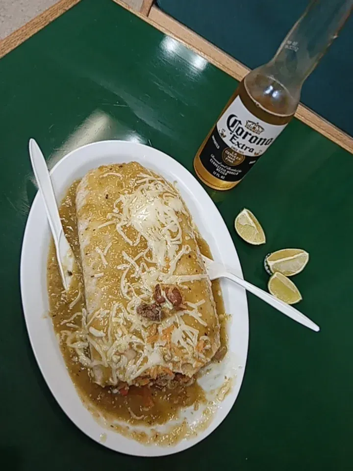 A burrito is on a plate next to a bottle of corona beer