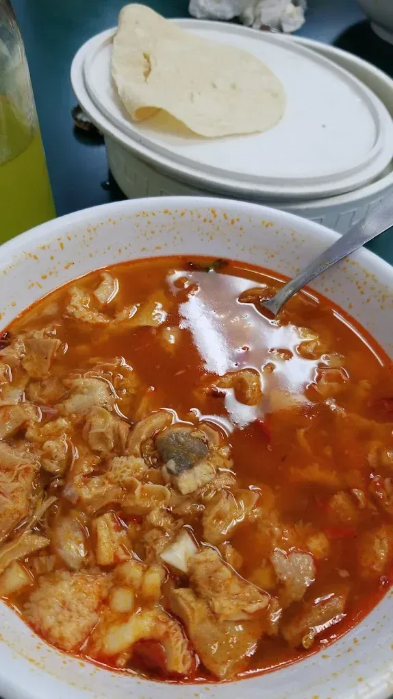 A bowl of soup with a spoon in it and a tortilla on the side.