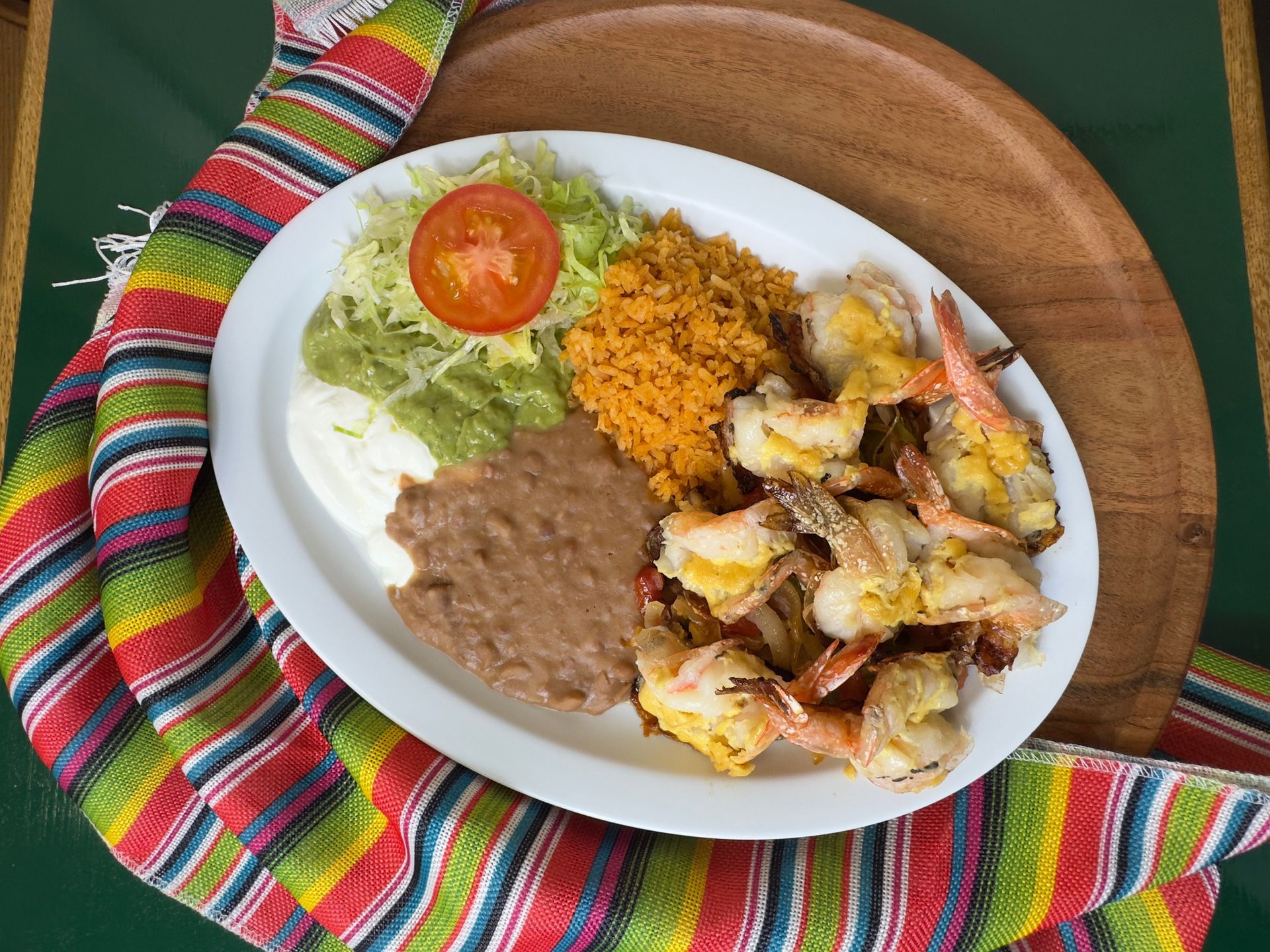 Grilled shrimp with rice, beans, guacamole, and toppings on a white plate.