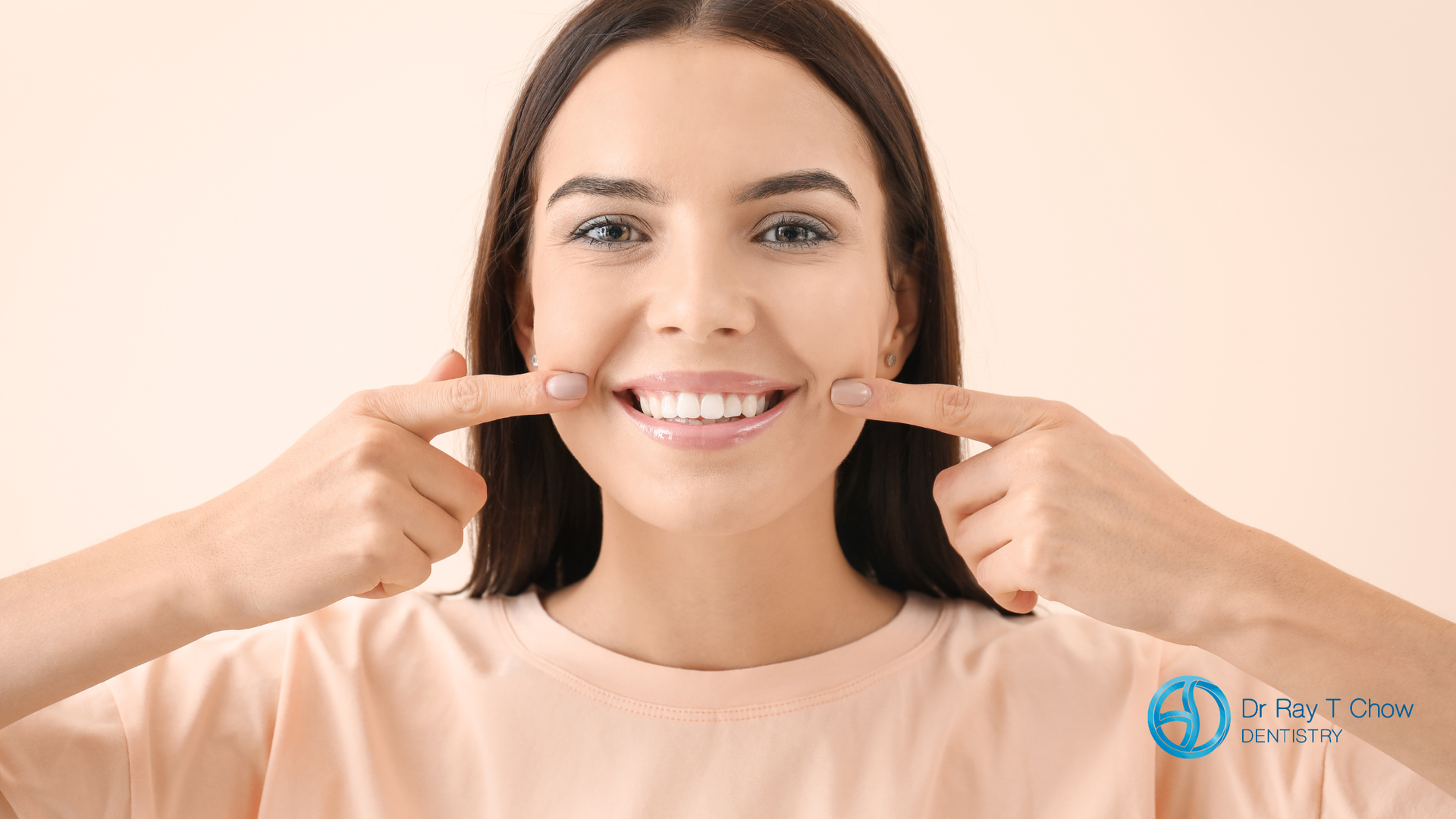 Woman pointing to her smiling teeth, light background.