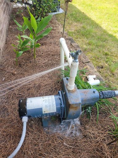 A water pump is sitting in the grass next to a house.