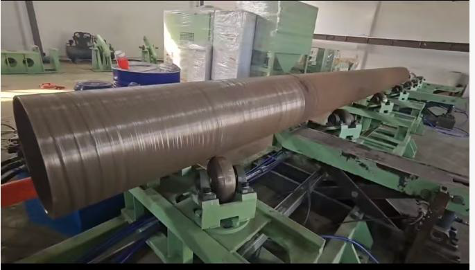 A large, cylindrical metal object is mounted on rollers in a workshop, likely for processing or manufacturing.