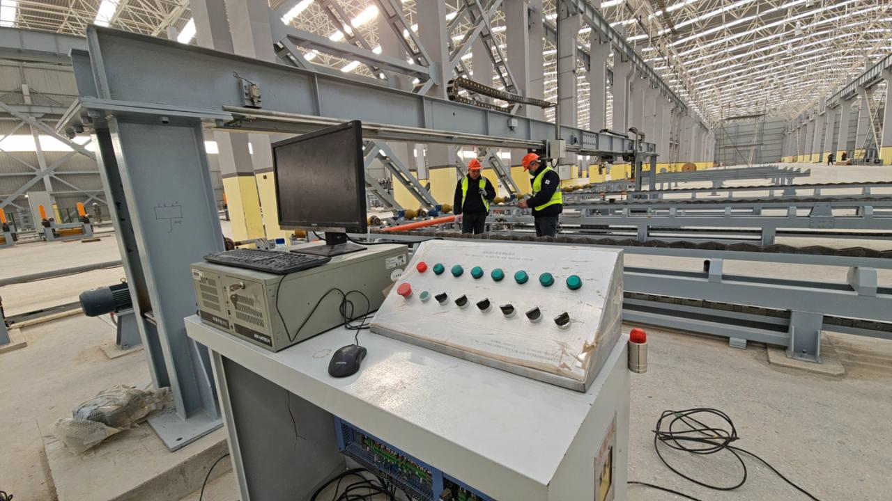 Control panel in a factory with two workers in safety vests. Computer monitor and buttons.
