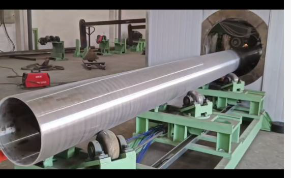 Large metal cylinder in a workshop being rotated by multiple rollers.